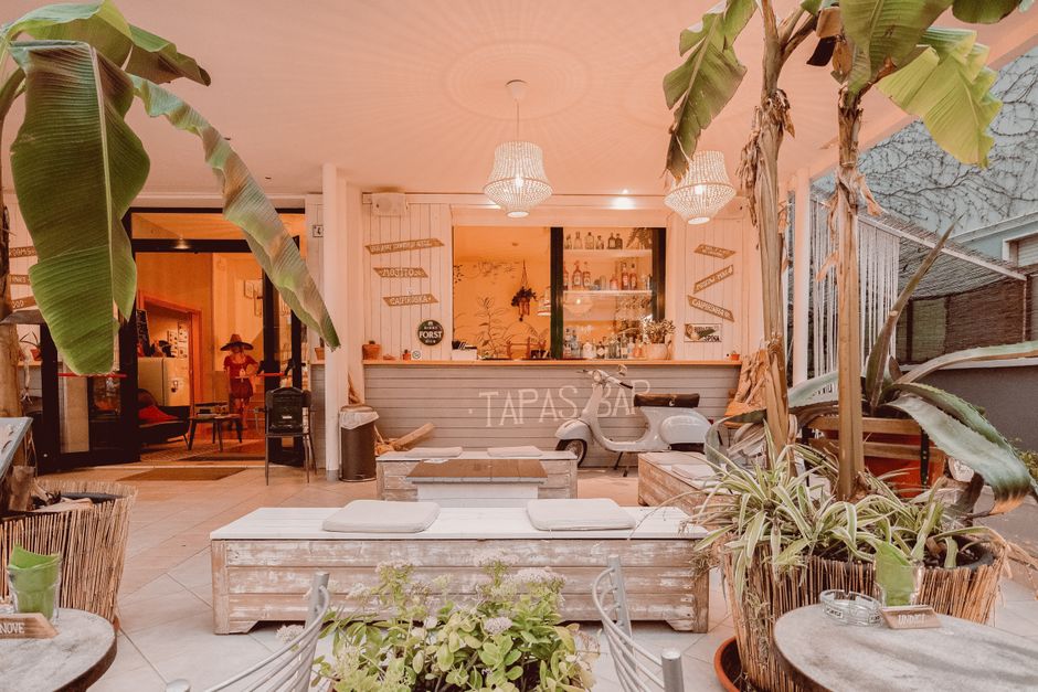 Warmly lit indoor tapas bar featuring tropical decor, wooden furniture, and hanging lights.