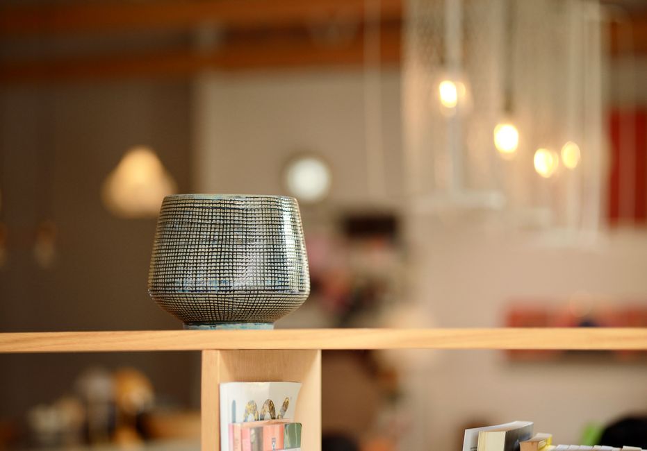 A stylish ceramic vase on a wooden shelf in a warmly lit interior setting.